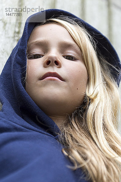Bildnis eines ernsthaften blonden Mädchens mit blauer Kapuzenjacke