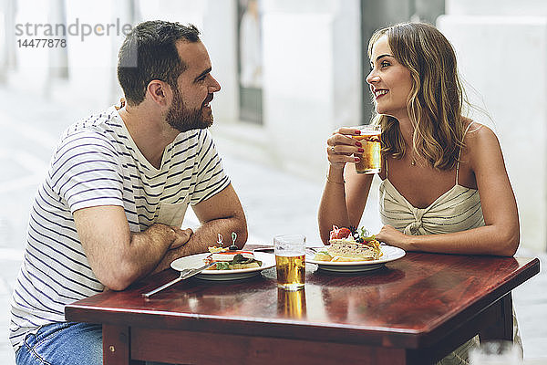 Lächelndes Paar isst und trinkt Bier in einem Restaurant auf der Straße