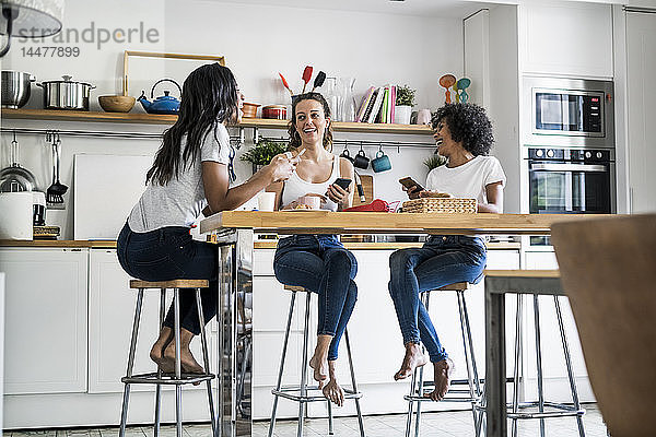 Drei glückliche Frauen sitzen zu Hause am Küchentisch und unterhalten sich