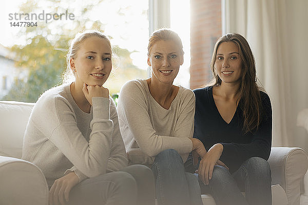 Porträt einer lächelnden Mutter mit zwei Mädchen im Teenager-Alter  die zu Hause auf der Couch sitzen