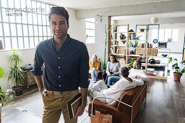 Porträt eines selbstbewussten jungen Geschäftsmannes mit Mitarbeitern im Hintergrund im Loft-Büro
