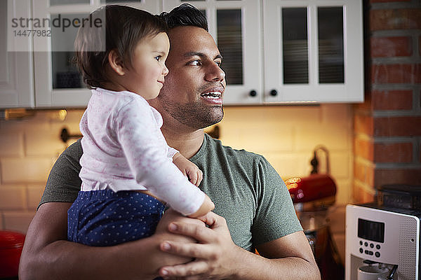 Vater hält kleines Mädchen zu Hause in der Küche