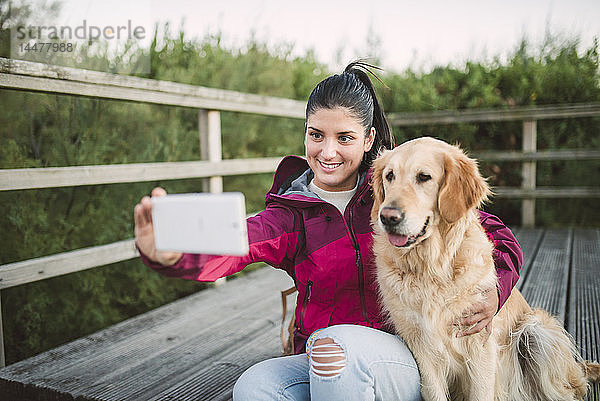 Lächelnde junge Frau  die mit ihrem Hund ein Selfie mitnimmt