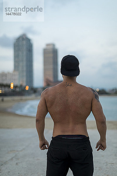 Rückansicht eines barbusigen  muskulösen Mannes am Strand in der Abenddämmerung