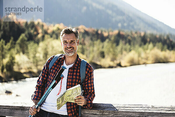 Österreich  Alpen  lächelnder Mann auf einer Wanderung mit Karte auf einer Brücke