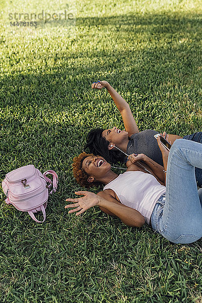 Zwei unbekümmerte Freundinnen entspannen sich in einem Park und hören Musik