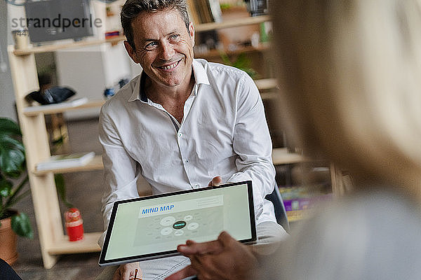 Lächelnder Geschäftsmann hält Tablett mit einer Mind Map während einer Präsentation im Loft-Büro