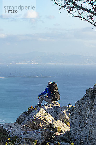 Spanien  Andalusien  Tarifa  Mann auf einer Wanderung an der Küste sitzend auf einem Felsen mit Aussicht