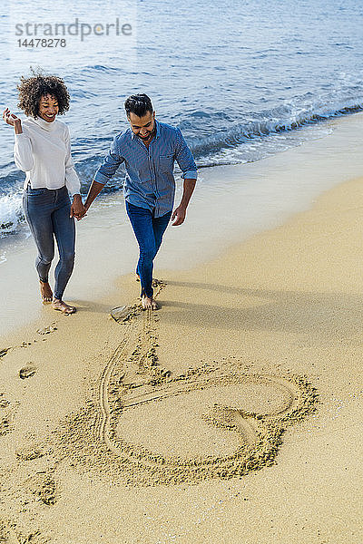 Spanien  Barcelona  glückliches Paar am Strand  das sich am Strand vergnügt und ein Herz in den Sand zeichnet