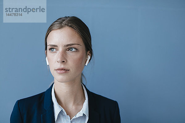 Porträt einer jungen Geschäftsfrau vor blauem Hintergrund  die Ohrknöpfe trägt