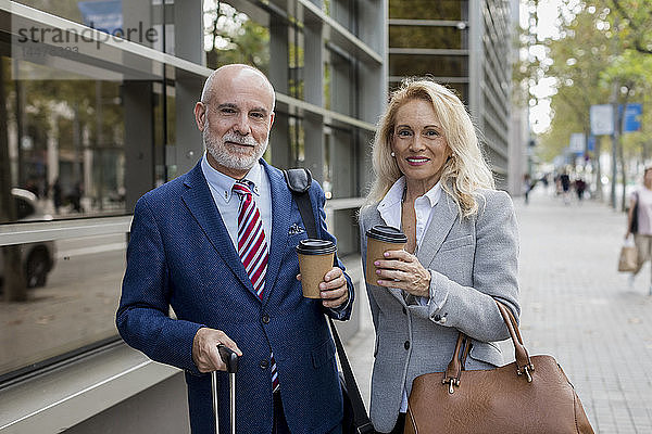 Porträt eines lächelnden älteren Geschäftsmannes und einer Geschäftsfrau mit Gepäck unterwegs in der Stadt