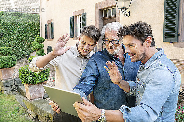 Drei Männer unterschiedlichen Alters bei einem Video-Chat per Tablet im Garten