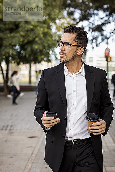 Geschäftsmann mit Kaffee zum Mitnehmen und Handy in der Stadt unterwegs
