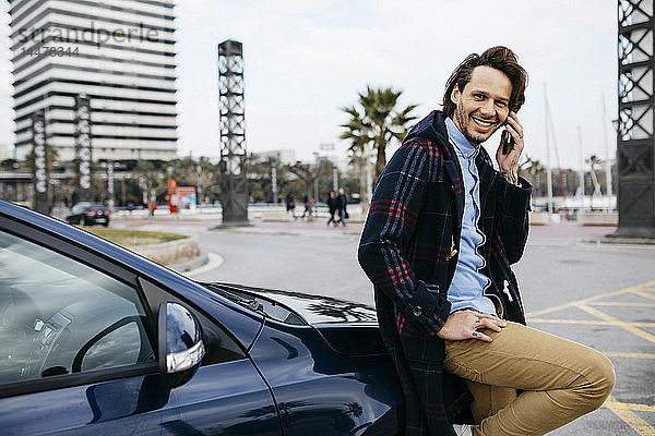 Spanien  Barcelona  lächelnder Mann am Handy vor dem Auto in der Stadt