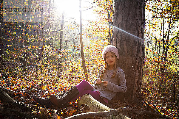 Junges Mädchen sitzt im Herbst auf einem Baum