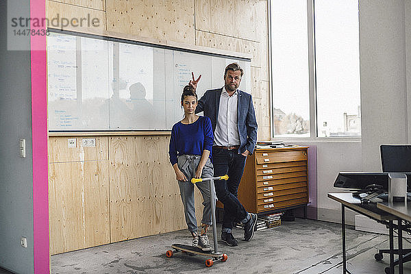 Ein reifer Mann und sein Assistent spielen mit einem Roller und stehen im Büro vor dem weißen Brett