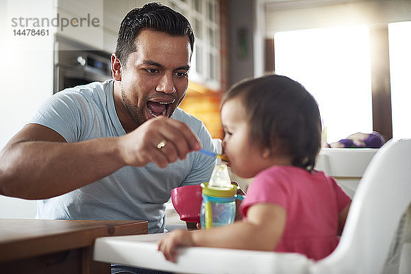 Vater füttert kleines Mädchen  das zu Hause im Hochstuhl sitzt