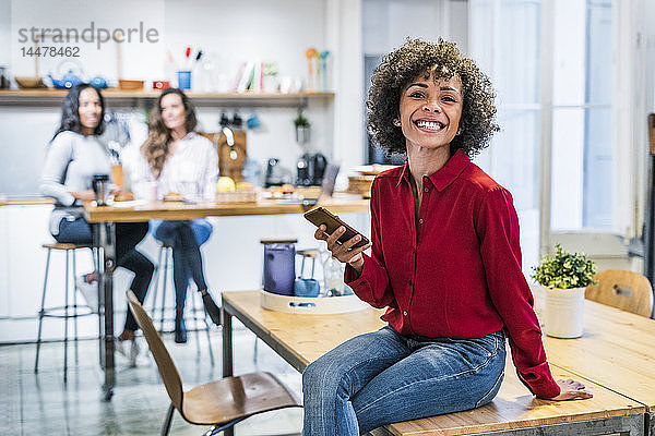 Porträt einer glücklichen Frau mit Handy auf dem Tisch sitzend