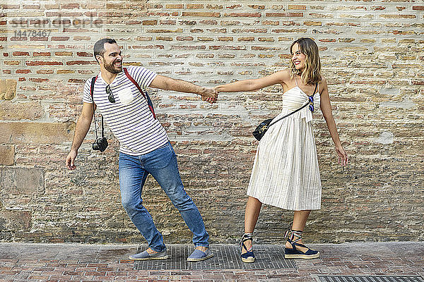 Glückliches Paar hält sich an der Ziegelmauer an den Händen und geht in entgegengesetzte Richtungen