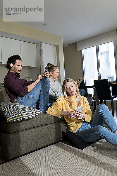 Gelangweilte Freunde sitzen auf der Couch im Wohnzimmer und benutzen digitale Geräte