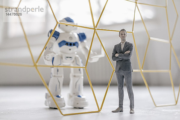 Miniatur-Geschäftsmann-Figur  die vor einem Roboter mit Laptop steht  der durch eine Struktur getrennt ist