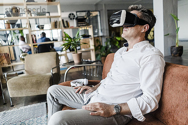 Reifer Mann mit VR-Brille sitzt auf einer Couch auf einem Dachboden