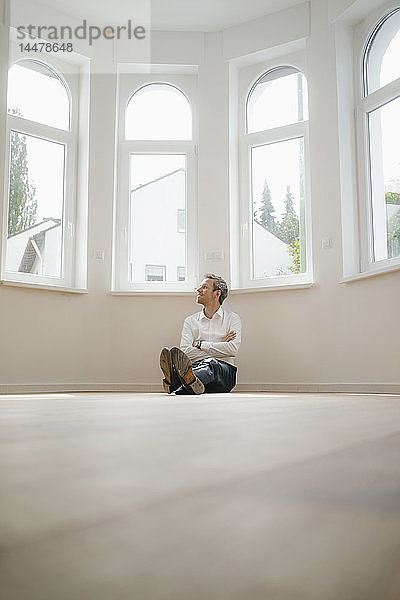 Geschäftsmann sitzt auf dem Boden seines frisch renovierten Hauses und sieht glücklich aus