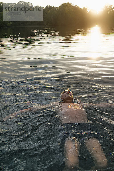 Älterer Mann schwimmt bei Sonnenuntergang in einem See