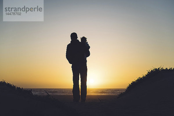 USA  Kalifornien  Morro Bay  Silhouetten von Vater und Baby beim Sonnenuntergang am Strand