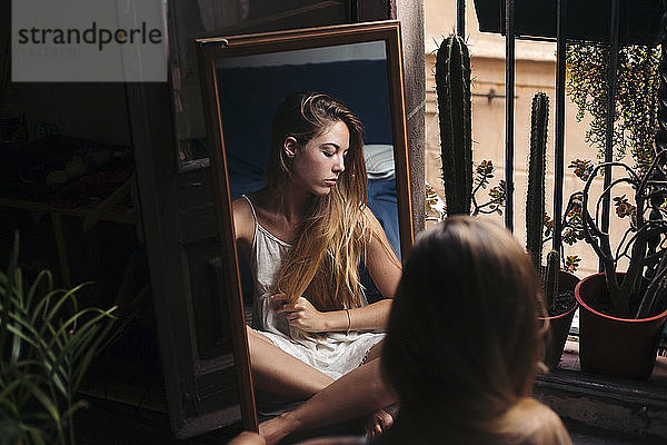 Spiegelbild einer jungen Frau  die zu Hause auf dem Boden sitzt und sich entspannt