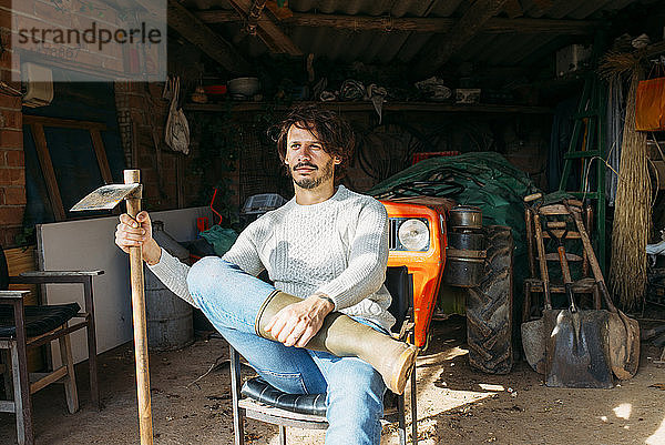Mann mit Hacke  der mit einem Traktor in einem Schuppen sitzt