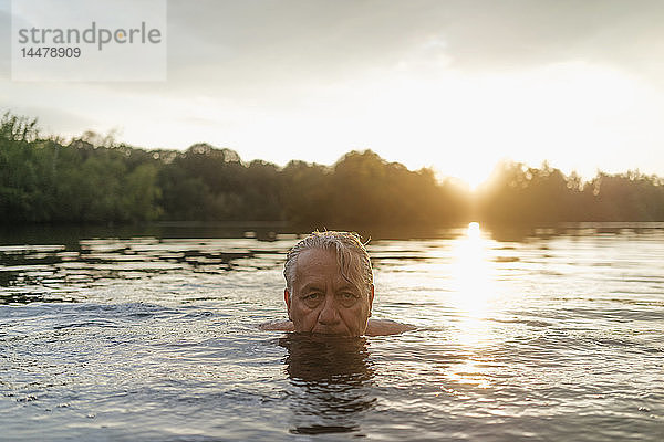 Älterer Mann schwimmt bei Sonnenuntergang in einem See