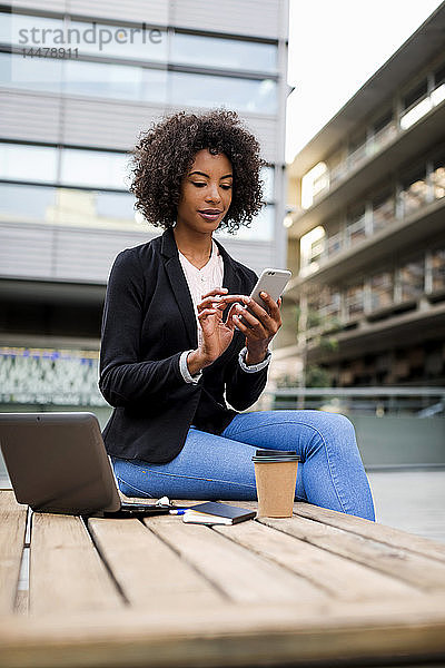 Porträt einer Geschäftsfrau  die im Freien mit einem Smartphone auf einem Tisch sitzt