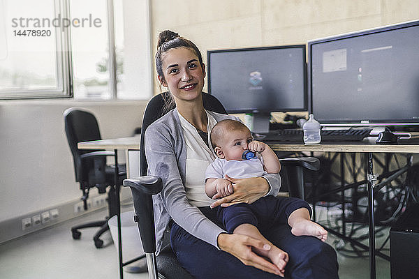 Berufstätige Mutter mit Baby auf dem Schoß  im Büro sitzend