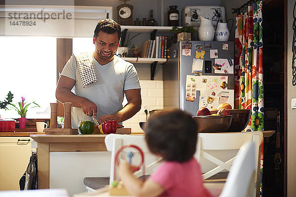 Lächelnder Vater bereitet zu Hause in der Küche Essen für seine Tochter zu