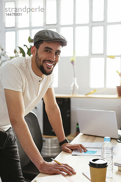 Porträt eines lächelnden jungen Mannes  der sich am Schreibtisch im Büro Notizen macht