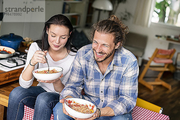 Glückliches Paar sitzt am Küchentisch und isst Spaghetti