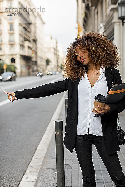 Junge Frau mit Laptoptasche und Kaffee zum Mitnehmen in der Stadt  ein Taxi rufend