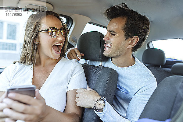 Glückliches Paar im Auto  das eine Grimasse zieht  mit Mann auf dem Rücksitz und Frau auf dem Beifahrersitz
