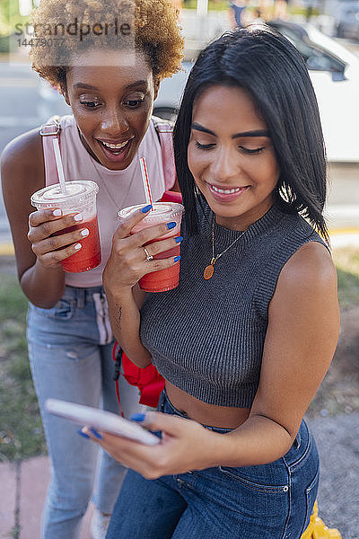 USA  Florida  Miami Beach  zwei glückliche Freundinnen mit Handy und Erfrischungsgetränk in der Stadt