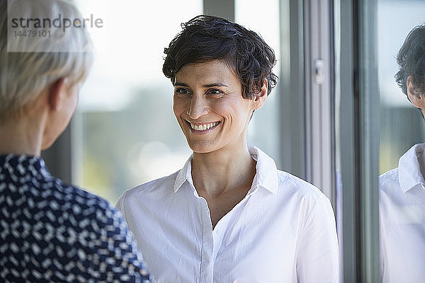 Porträt einer lächelnden Geschäftsfrau  die ihren Kollegen am Fenster im Büro ansieht