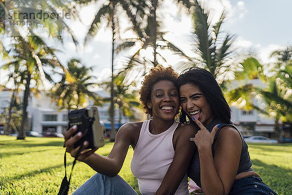 Zwei glückliche Freundinnen machen ein Sofortfoto in einem Park