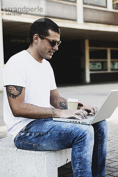 Junger Mann sitzt mit Laptop im Freien