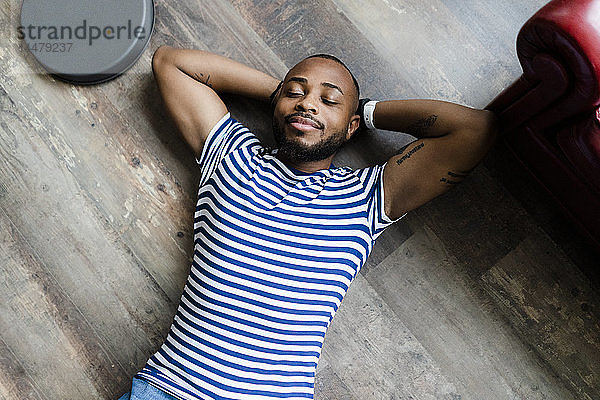 Lächelnder junger Mann mit geschlossenen Augen auf Holzboden liegend