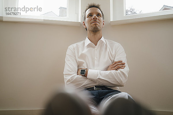 Geschäftsmann mit Smartwatch sitzt auf dem Boden seiner Wohnung und träumt