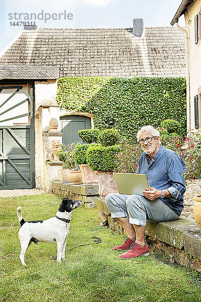 Porträt eines lächelnden älteren Mannes mit Hund im Garten mit Tablette