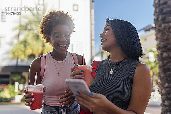 USA  Florida  Miami Beach  zwei glückliche Freundinnen mit Handy und Erfrischungsgetränk in der Stadt