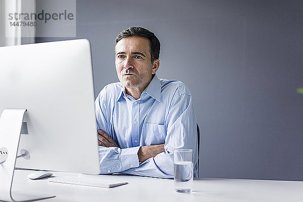 Seriöser Geschäftsmann  der im Büro am Schreibtisch sitzt und auf den Computerbildschirm schaut