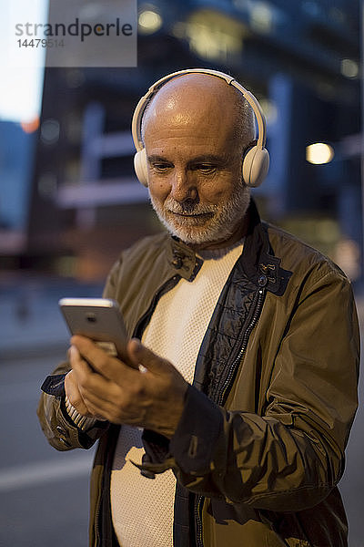Spanien  Barcelona  älterer Mann mit Kopfhörern und Handy in der Stadt in der Abenddämmerung