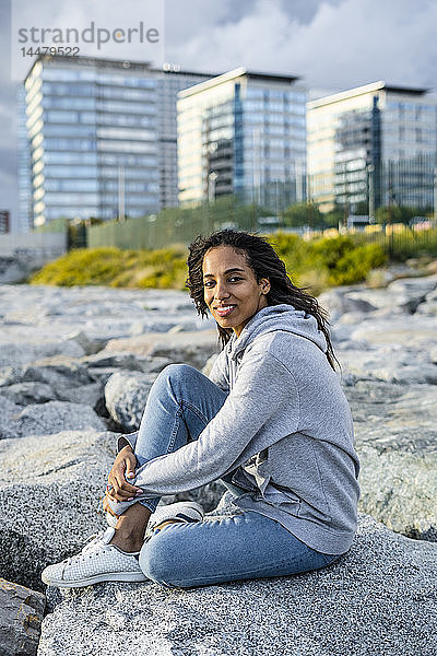 Junge Frau sitzt auf Felsen am Strand und entspannt